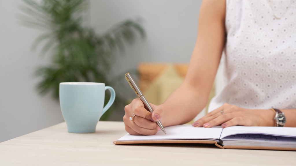 A woman journaling at her desk to track and identify the real source of her workplace stress.