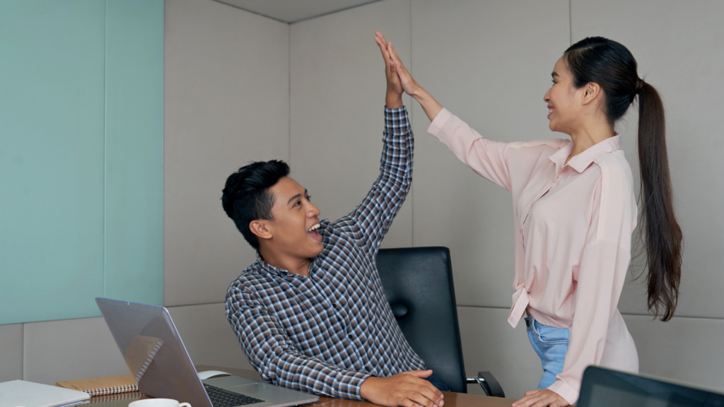 Two coworkers high-fiving in the office, representing how supportive leadership and a positive workplace culture help reduce employee stress.